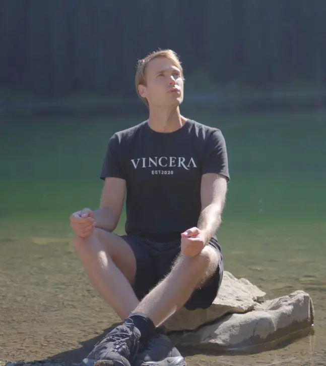 zittende man bij het water blaast uit, draagt een zwart vincera shirt