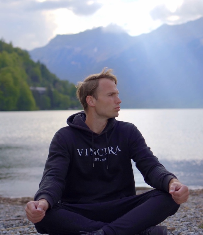 zittende man bij een Zwitsers meer doet een ademhalingsoefening, draagt een zwart vincera trui
