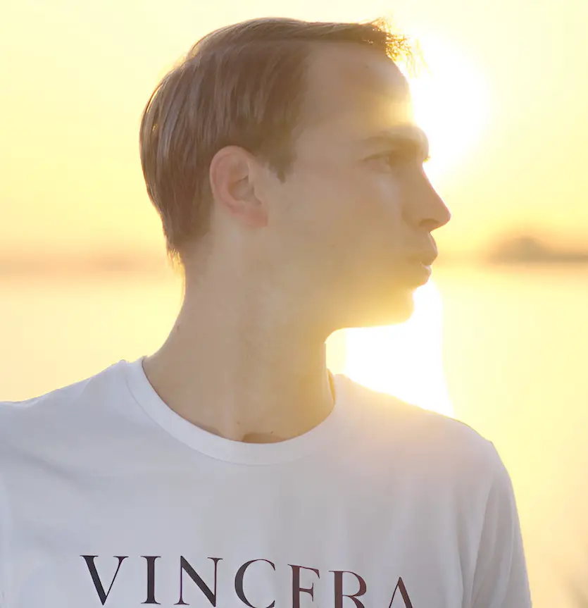 man doet ademhaling met getuite lippen bij het water tijdens de zonsopkomst, draagt een wit vincera shirt
