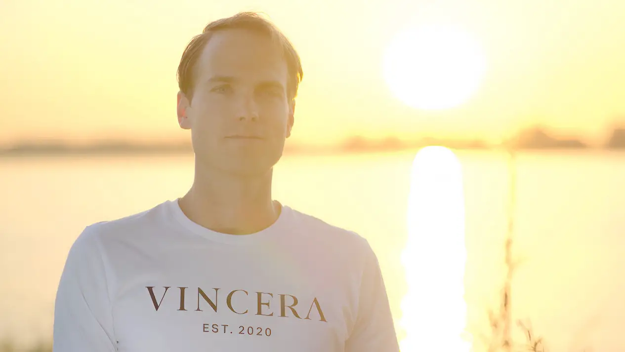 man doet een ademhalingsoefening en kijkt in de camera tijdens de zonsopkomst, draagt een wit vincera shirt