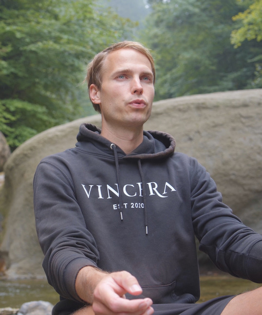 Een zittende man, buiten in zijn Vincera sweater in de natuur, doet Mindfulness Ademhalingsoefeningen