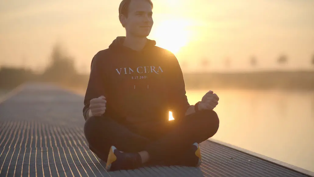 zittende man bij zonsopkomst doet de 4 7 8 ademhaling, draagt een zwarte vincera trui en een zwarte broek