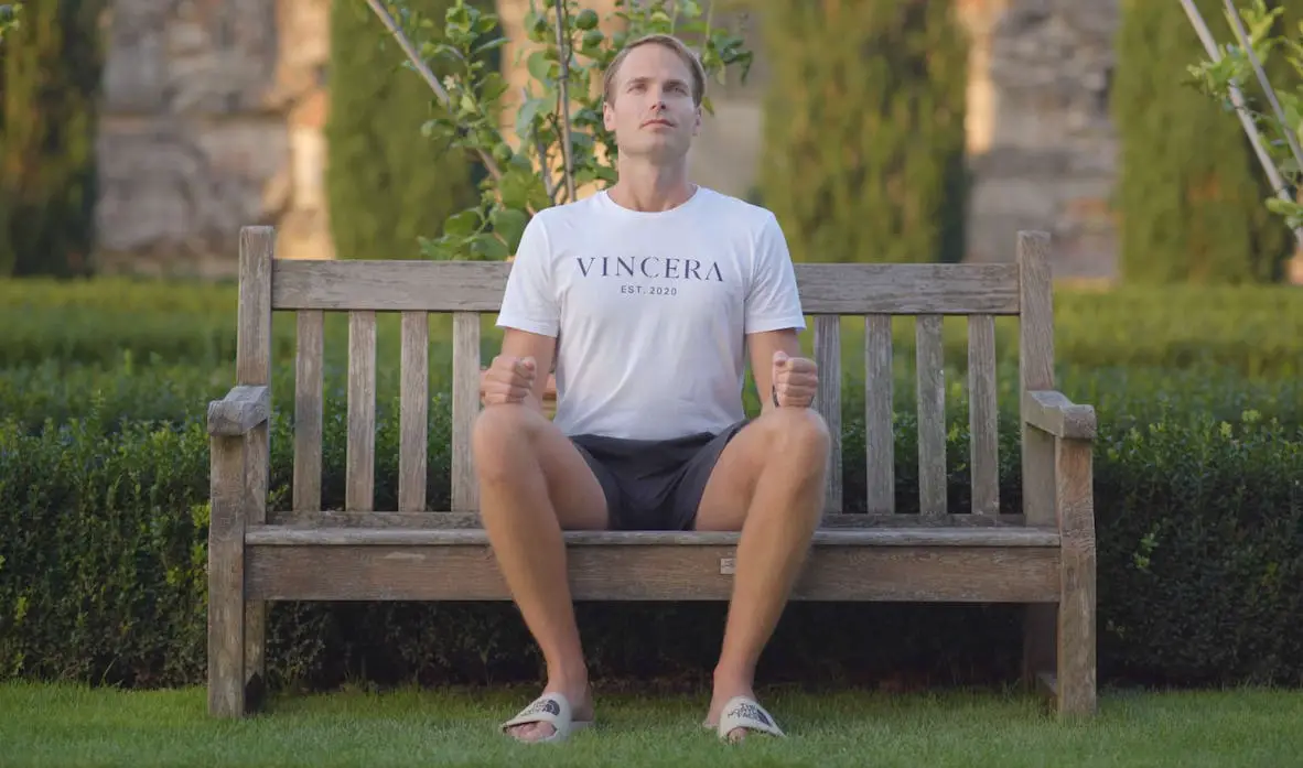 adem inhouden door een man die buiten op een bankje zit, draagt een wit vincera shirt