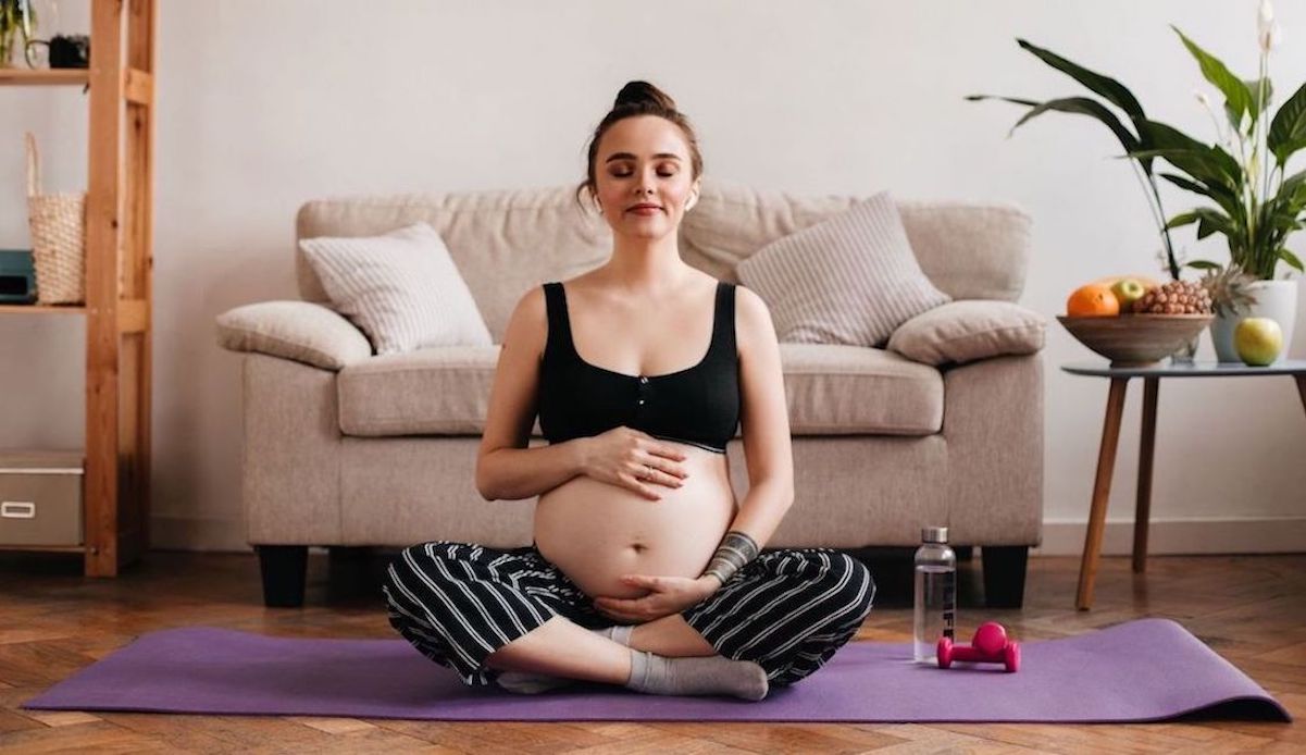 jonge zwangere vrouw doet binnen zwangerschap ademhalingsoefeningen met haar handen op haar buik