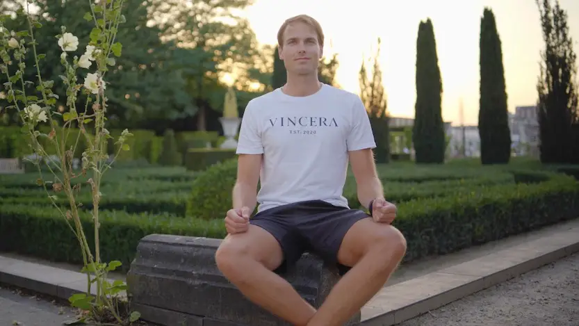 zittende man in een mooie tuin doet ademhalingsoefeningen tegen misselijkheid, draagt een wit vincera shirt