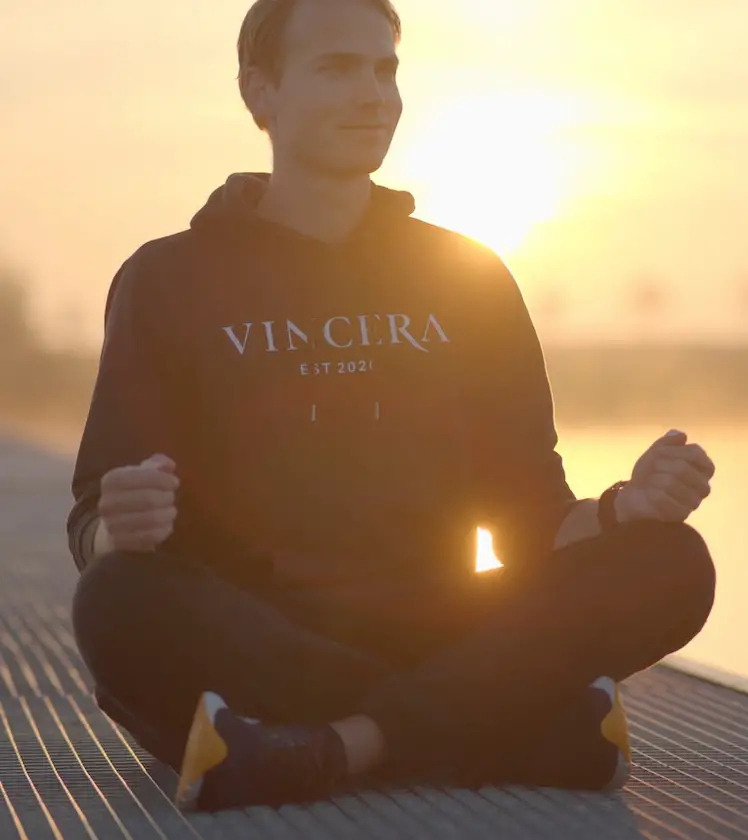 Man zit en doet de 4 7 8 ademhaling tijdens de zonsopkomst, draagt een zwart vincera vest