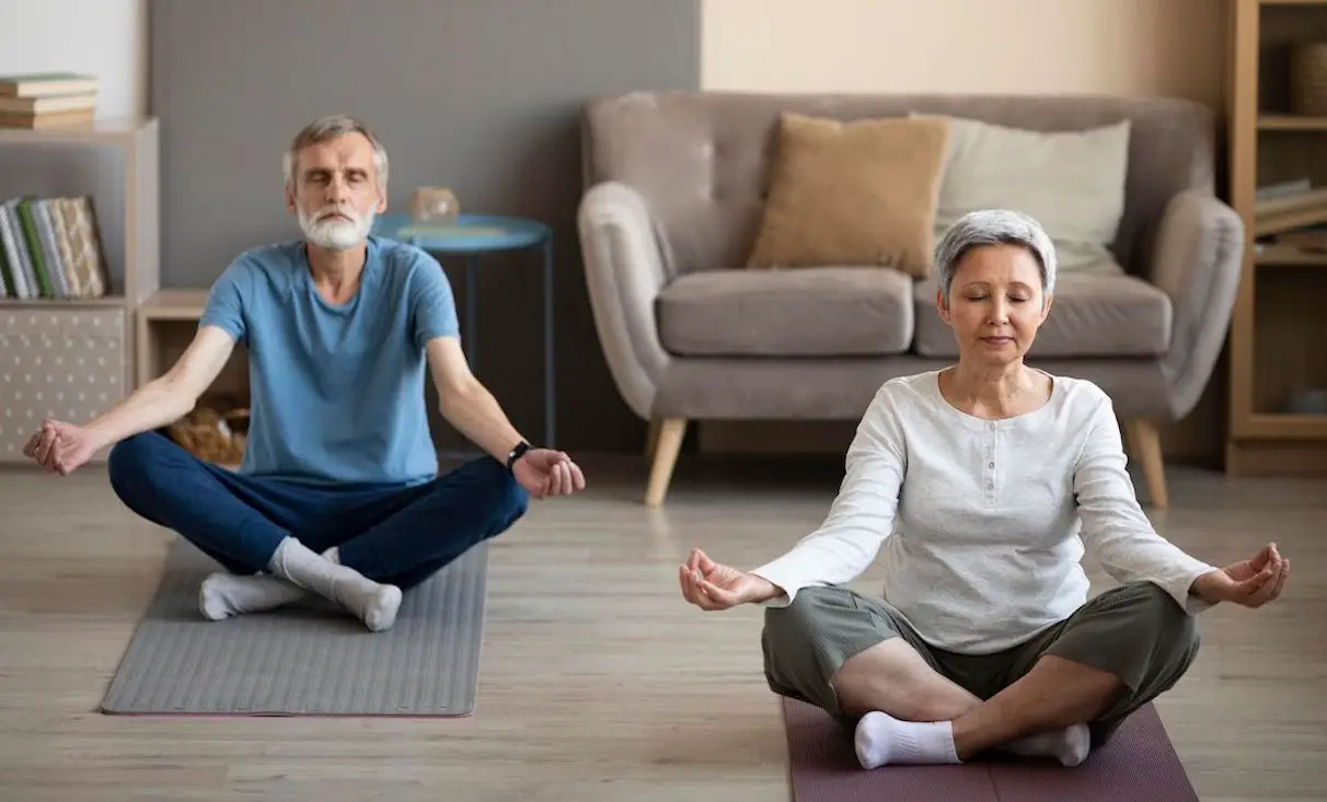 oudere man en vrouw zitten in een kamer en doen ademhalingsoefeningen tegen hoge bloeddruk